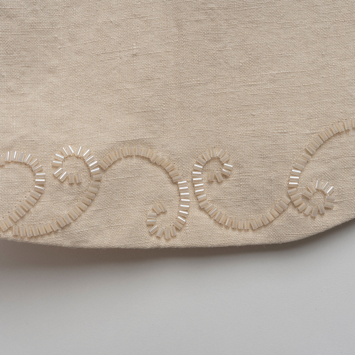 Close-up of beige fabric with decorative embroidery on a light gray background