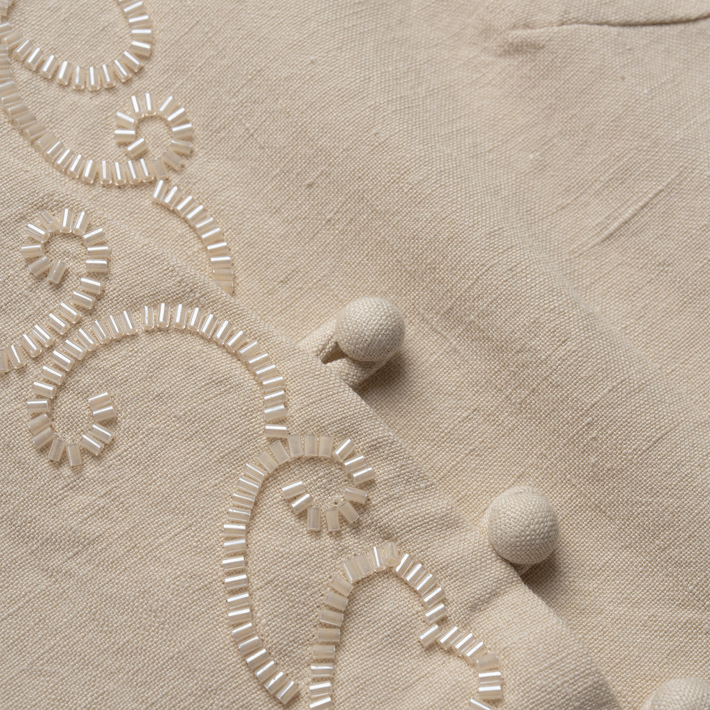 Close-up of beige vest with embroidered patterns and pom-poms.