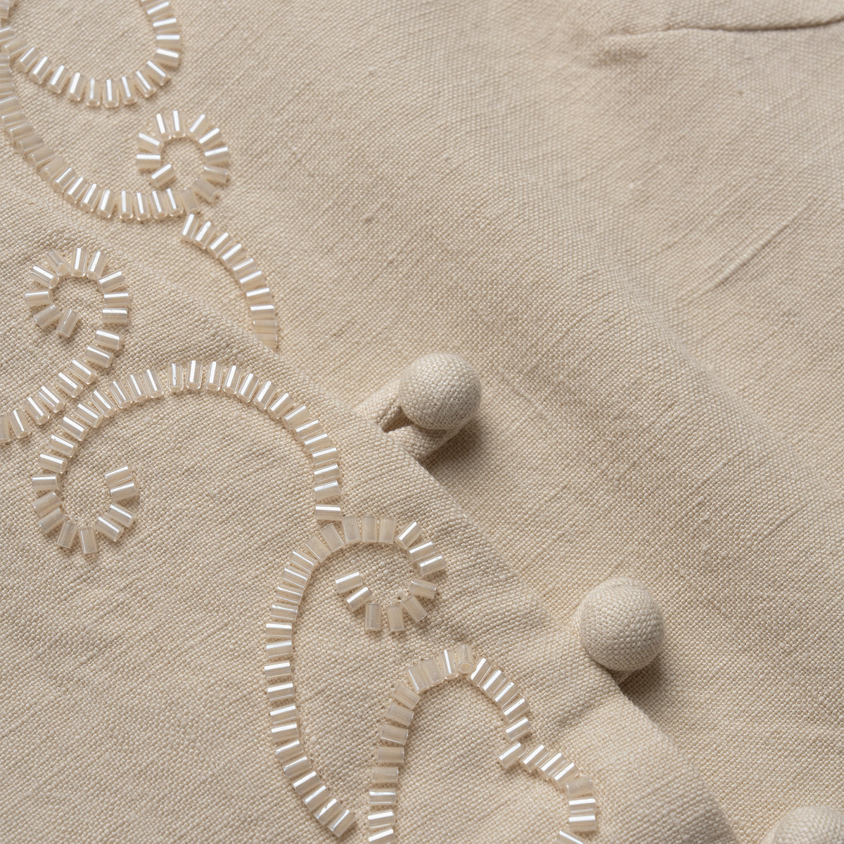 Close-up of beige vest with embroidered patterns and pom-poms.
