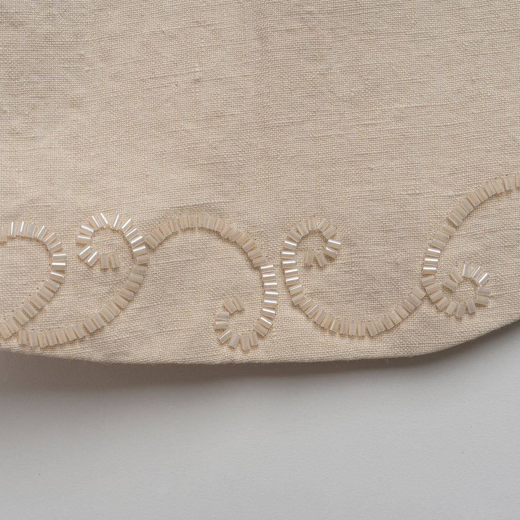 Close-up of beige fabric with decorative embroidery on a light gray background