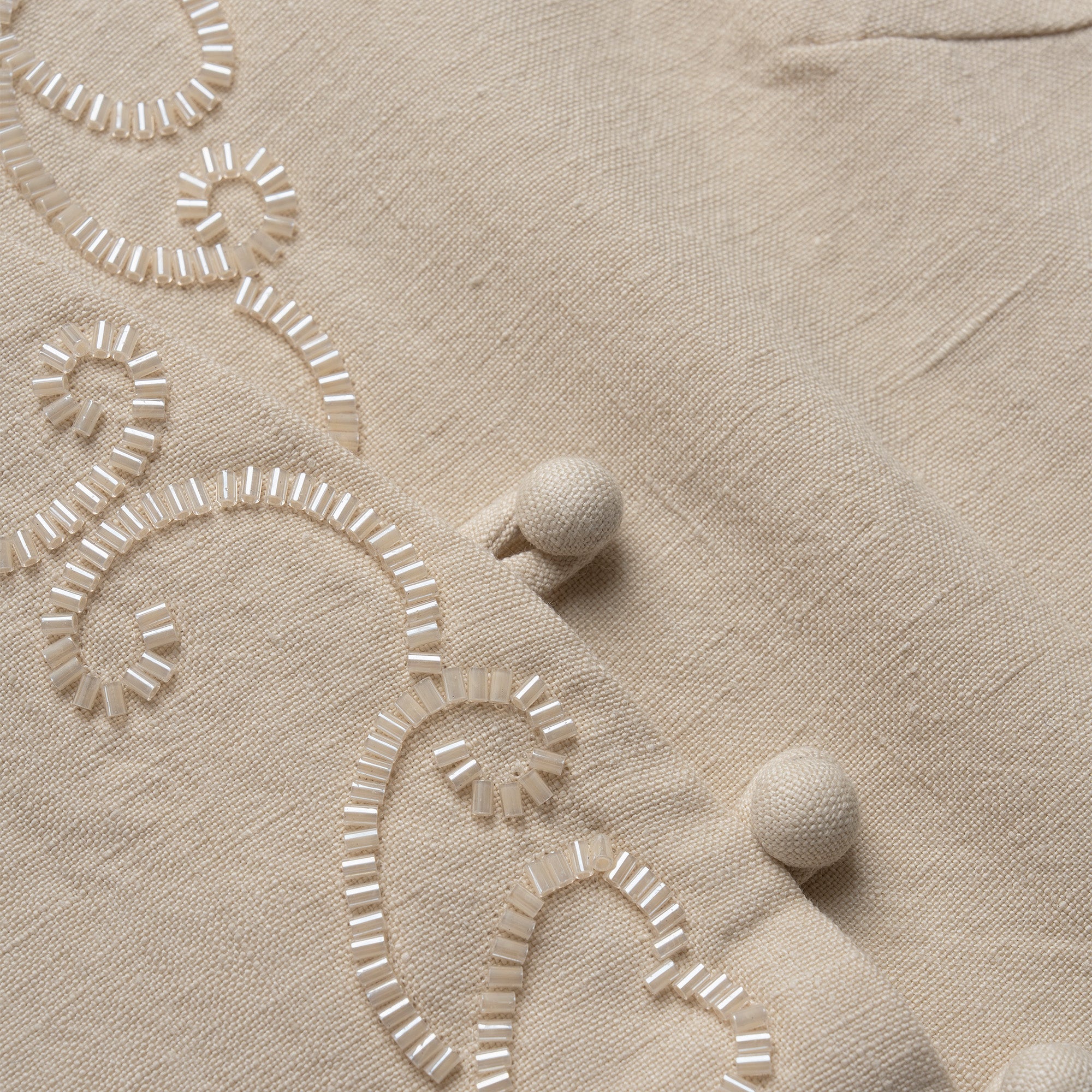 Close-up of beige vest with embroidered patterns and pom-poms.