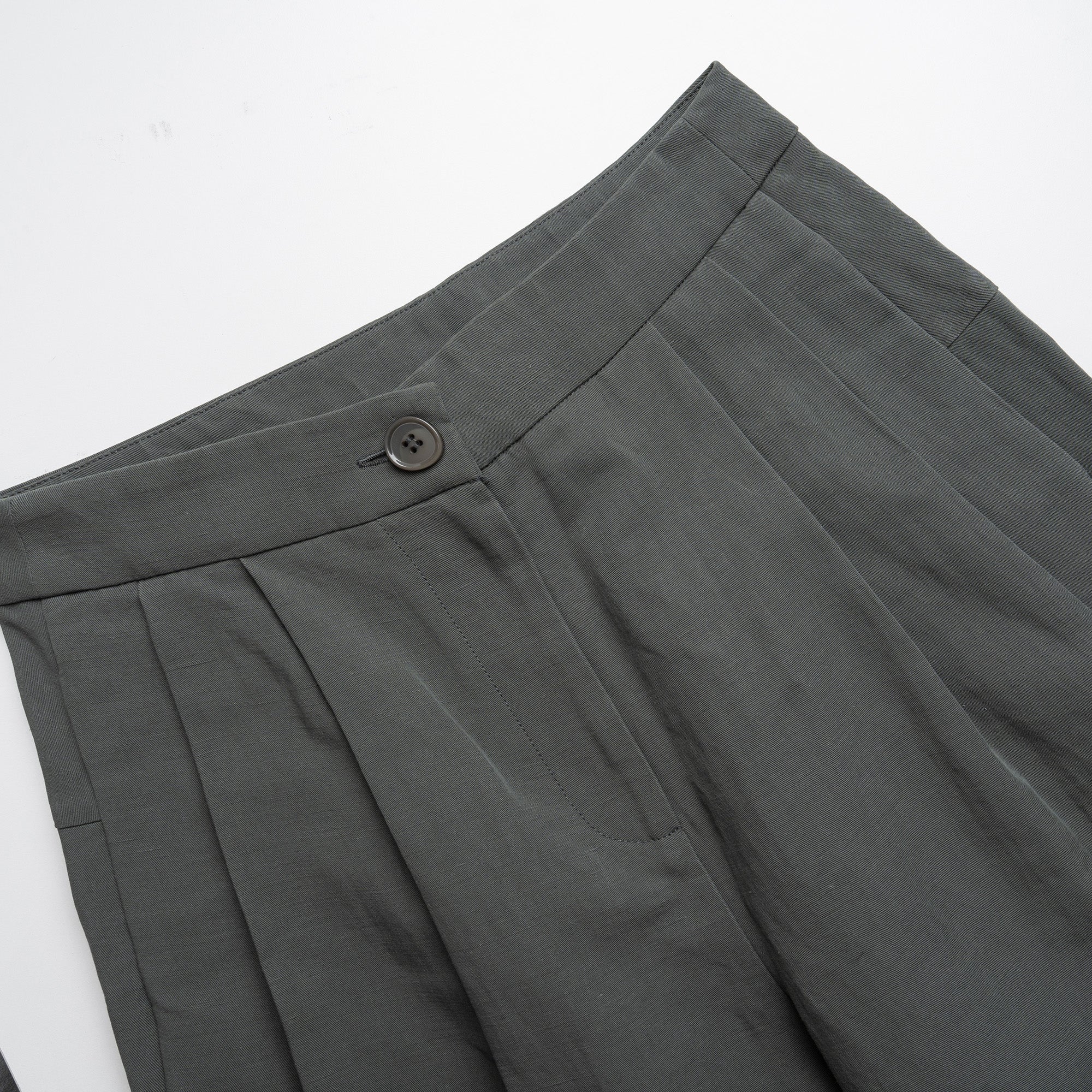 Close-up of moss green pleated pants with a button on a white background