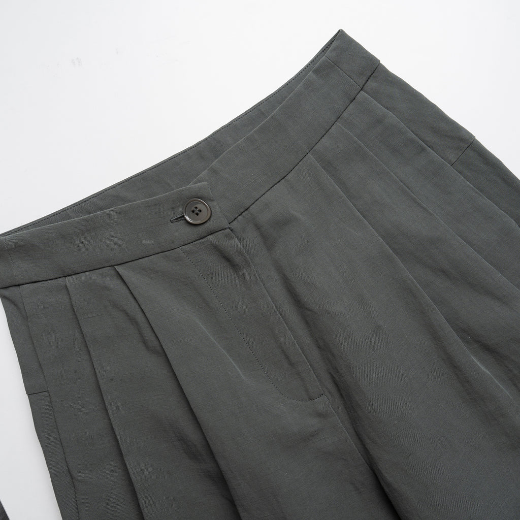 Close-up of moss green pleated pants with a button on a white background