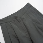 Close-up of moss green pleated pants with a button on a white background
