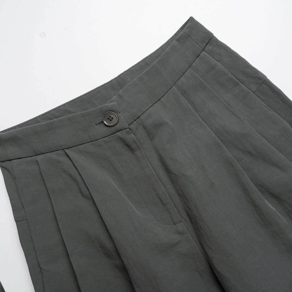 Close-up of moss green pleated pants with a button on a white background