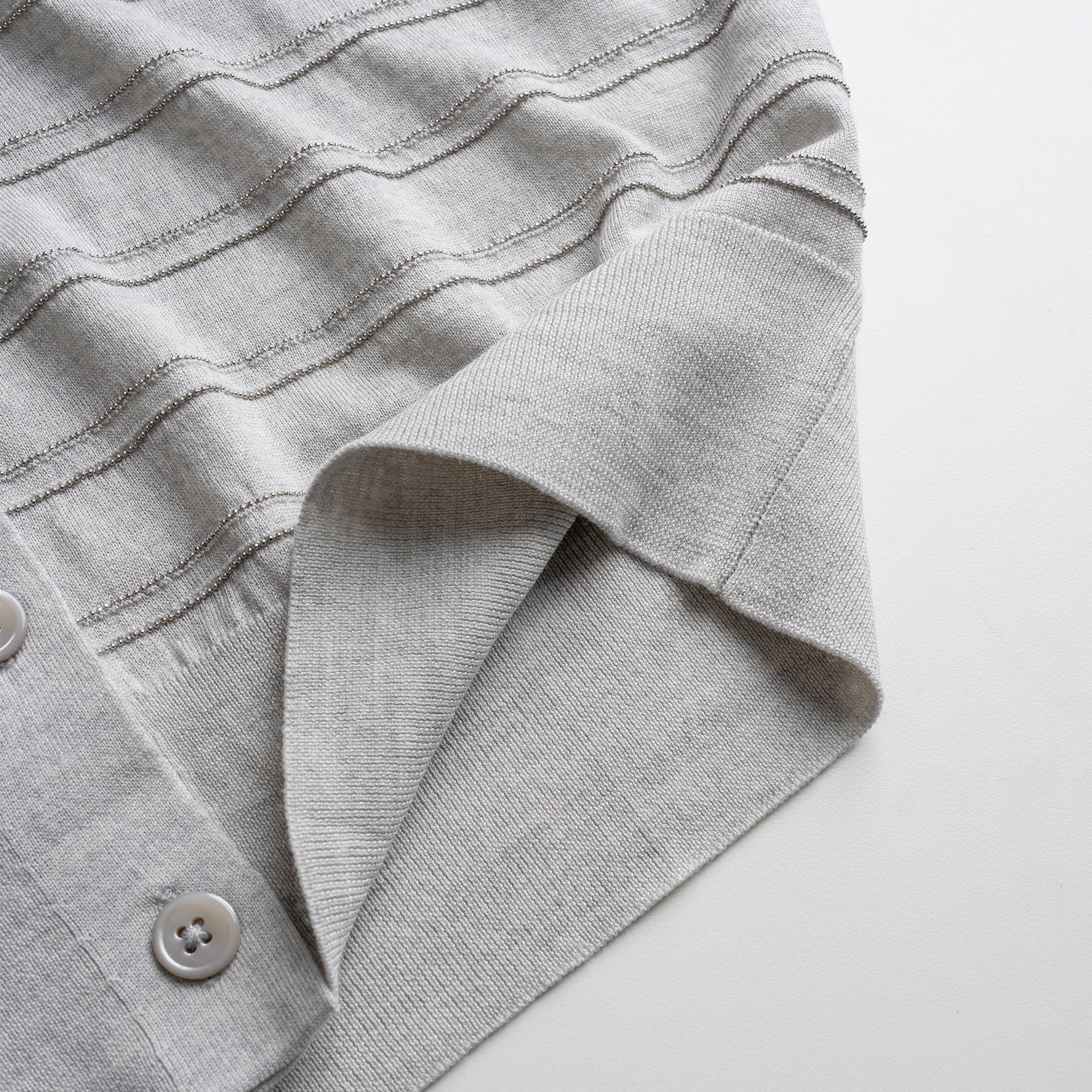 Close-up of a gray textured cardigan with a button on a white background
